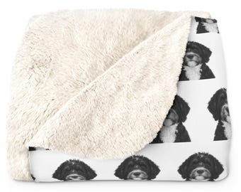 May include: A white and black sherpa blanket featuring a repeating pattern of a black and white dog's face. The blanket has a soft, fluffy texture on one side and a printed design on the other.