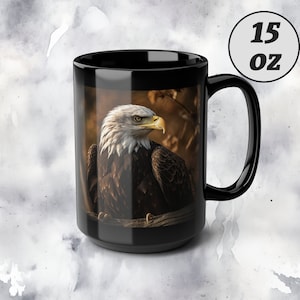 Puede incluir: Taza de cerámica negra con una capacidad de 15 oz que presenta una imagen de primer plano de un águila calva con plumaje marrón y blanco, mirando hacia la izquierda. El águila está posada en una rama con un fondo borroso de árboles y hojas.