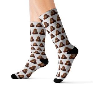 Könnte beinhalten: Ein Paar weiße Socken mit einem sich wiederholenden Muster aus Orang-Utan-Gesichtern. Die Socken sind oben und unten schwarz.