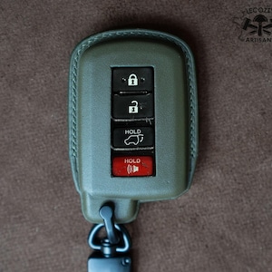 May include: A green leather key fob with a black key chain. The key fob has five buttons: lock, unlock, hold, trunk release, and panic. The buttons are labeled with white text.