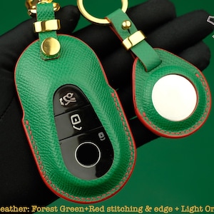 May include: A green leather key fob with red stitching and a gold metal ring. The key fob has a mirror on the back and the text "LECOZZY ARTISANS" is visible in the top right corner of the image.