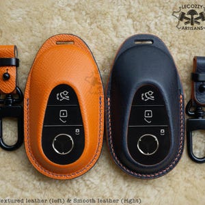 May include: Two key fobs, one with textured orange leather and one with smooth black leather. Both have a black key fob insert with buttons and a circular button. The key fobs have a black metal ring attached.