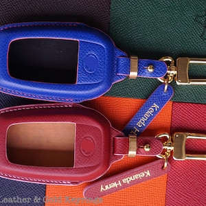 May include: Two leather keychains with gold hardware and a blue and red color scheme. The keychains have a small window for a key fob and a gold clasp. The keychains are labeled "Keyanda Henry".