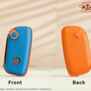May include: A blue and orange leather key fob with a textured finish. The front of the fob has a button and a small circular cutout. The back of the fob is plain.