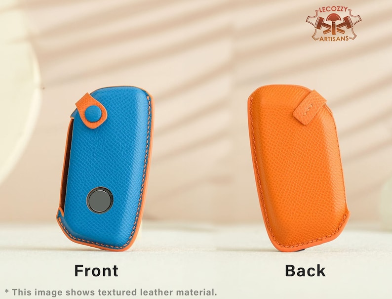 May include: A blue and orange leather key fob with a textured finish. The front of the fob has a button and a small circular cutout. The back of the fob is plain.
