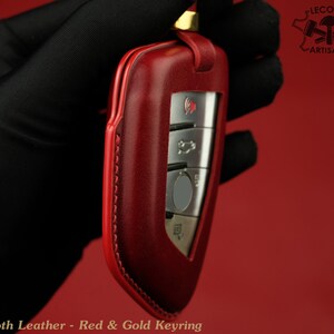 May include: Red leather key fob with gold accents and stitching. The fob has a silver key with buttons.  "Lecozzy Artisans" is printed on the top right corner of the image.