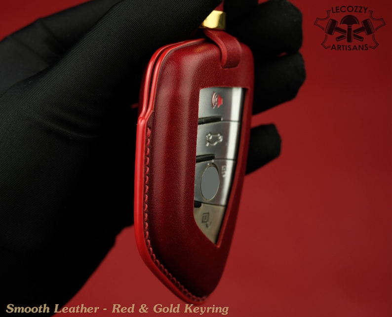 May include: Red leather key fob with gold accents and stitching. The fob has a silver key with buttons.  "Lecozzy Artisans" is printed on the top right corner of the image.
