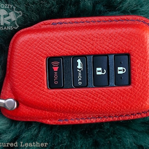 May include: Red leather key fob with a blue stitching detail. The fob has five buttons with icons for hold, unlock, and lock. The text "*Textured Leather" is visible at the bottom of the image.
