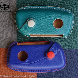 May include: Two leather key covers, one teal and one blue, with contrasting stitching. The teal cover has a white button and the blue cover has a red button. Both covers have a cutout for a key. *Textured Leather & Style B*