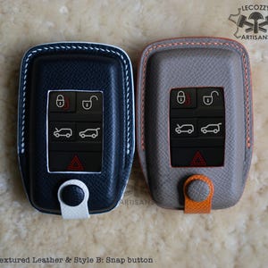 May include: Two key fobs with textured leather covers. One is navy blue with white stitching and the other is gray with orange stitching. Both have a snap button closure. "Lecozzy Artisans" is printed on the image.