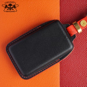 May include: Black leather key fob with red stitching and a gold metal ring. The fob is on a background of orange and red leather.