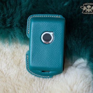 Peut inclure: Un étui de téléphone en cuir bleu sarcelle avec un bord cousu et une petite découpe circulaire pour l'objectif de l'appareil photo.