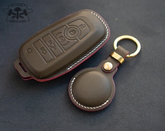May include: A dark brown leather key fob cover and matching round key ring holder. Both items have white stitching and a red edge. The key fob cover has embossed buttons. The key ring holder has a gold-colored ring.