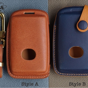 Puede incluir: Dos estuches de cuero para llaveros, uno marrón y otro azul, con un llavero unido al estuche marrón. El estuche marrón tiene el texto "Style A" debajo y el estuche azul tiene el texto "Style B" debajo.