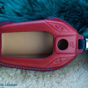 May include: Red leather key fob with blue stitching and a black strap. The fob has a cutout for a key and a small hole for a button. The text "Smooth Leather" is visible at the bottom of the image.