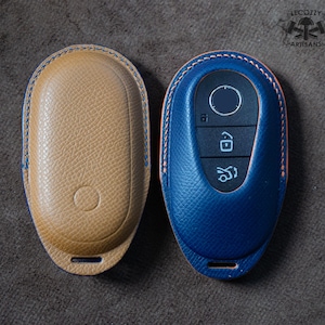Puede incluir: Dos fundas de llave de cuero, una en color tostado y otra en azul. La funda azul tiene un llavero dentro con botones para bloquear, desbloquear y abrir el maletero.