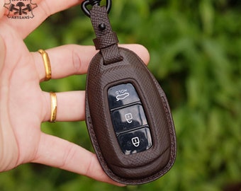 Könnte beinhalten: Ein brauner Leder-Schlüsselanhänger mit einem schwarzen Schlüssel im Inneren. Der Schlüsselanhänger hat drei Knöpfe: "HOLD", "Entriegeln" und "Verriegeln".