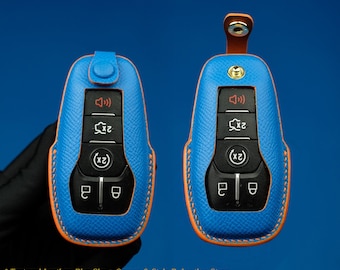 May include: A blue leather key fob with orange stitching. The key fob has a textured surface and features buttons for lock, unlock, and panic. The text "2x" is printed on the buttons.  *Textured Leather: Blue Sky + Orange & Style B: Leather Strap*