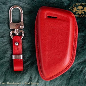May include: Red leather key fob with a silver key ring and strap. The fob has a stitched edge and is designed to fit a car key. The text "Lecozzy Artisans" is visible in the top right corner of the image.