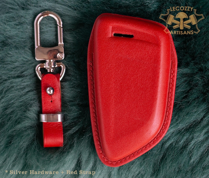 May include: Red leather key fob with a silver key ring and strap. The fob has a stitched edge and is designed to fit a car key. The text "Lecozzy Artisans" is visible in the top right corner of the image.