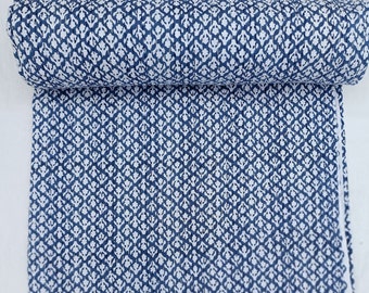 May include: A blue and white kantha quilt with a floral pattern. The quilt is rolled up and the fabric is visible.