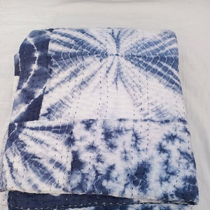 May include: A blue and white tie-dye kantha quilt with a circular pattern. The quilt is folded in thirds and has a white background with blue tie-dye swirls.