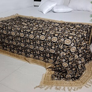 May include: Black and cream floral patterned throw blanket with a fringe border. The blanket is draped over a bed with white pillows.