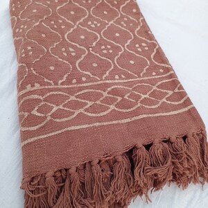 May include: A brown cotton throw blanket with a white geometric pattern and fringe trim.