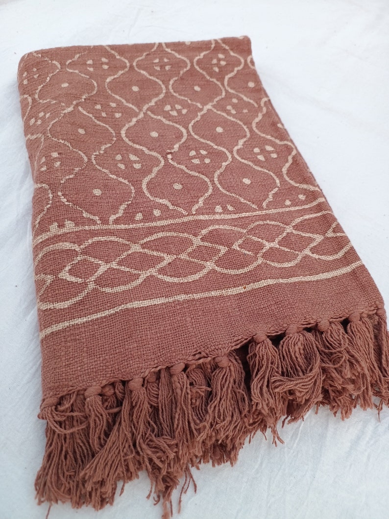 May include: A brown cotton throw blanket with a white geometric pattern and fringe trim.