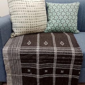 Puede incluir: Una manta de tiro negra y blanca con flecos en un sofá azul con dos almohadas estampadas. Una almohada es blanca con puntos grises y la otra es verde con un patrón geométrico.
