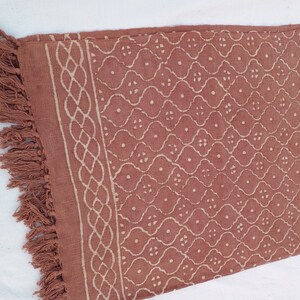 May include: A rust-colored cotton throw blanket with a white geometric pattern and fringe on the edges.