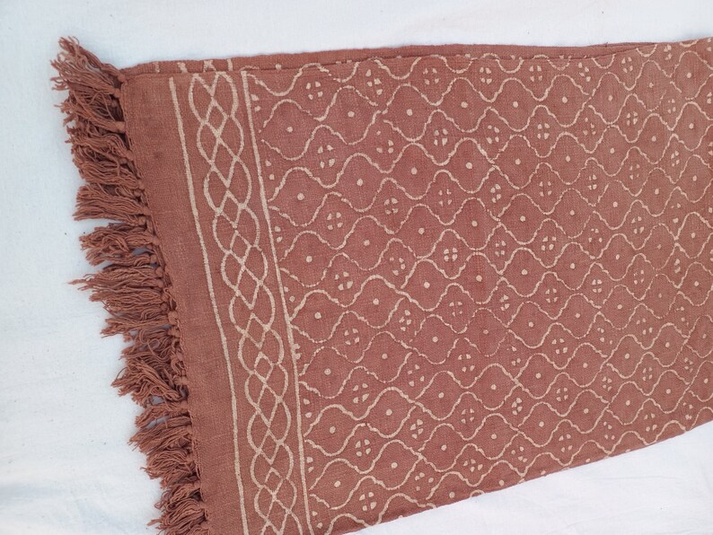 May include: A rust-colored cotton throw blanket with a white geometric pattern and fringe on the edges.