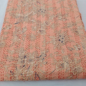 May include: A peach-colored quilt with a floral pattern in beige and dark blue. The quilt is hand-stitched with red thread, creating a textured surface. The overall design is a mix of botanical and abstract shapes.