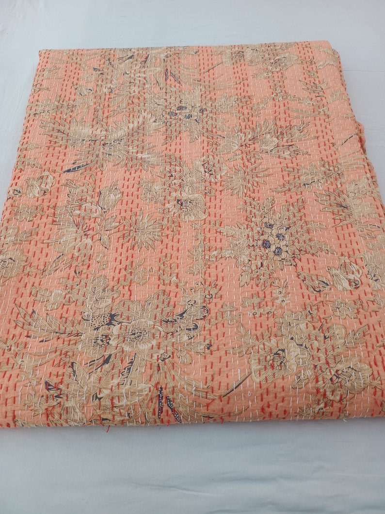 May include: A peach-colored quilt with a floral pattern in beige and dark blue. The quilt is hand-stitched with red thread, creating a textured surface. The overall design is a mix of botanical and abstract shapes.