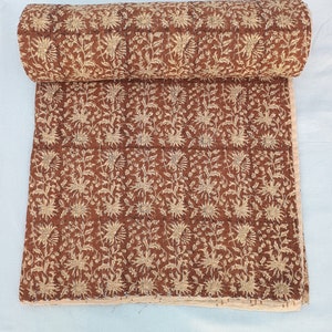 May include: A brown cotton quilt with a white floral pattern. The quilt is rolled up and the floral pattern is visible on the fabric.
