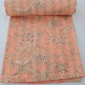 May include: A rolled-up peach-colored quilt with a floral pattern in beige and blue. The quilt is hand-stitched with white thread, and the edges are finished with a red stitch.
