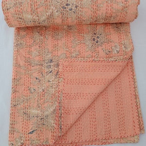 May include: A peach-colored quilt with a floral pattern in beige and navy blue. The quilt is hand-stitched with red thread, and the edges are neatly finished. The quilt is folded and rolled, showcasing the intricate design and craftsmanship.