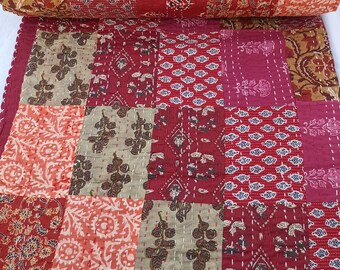 Op de afbeelding: Een rood, oranje en bruin patchwork-deken met een bloemenprint. Het deken is gemaakt van katoen en is met de hand gestikt. Het is een traditioneel Indiaas deken.