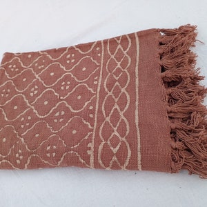 May include: A brown cotton throw blanket with a white geometric pattern and fringe trim.