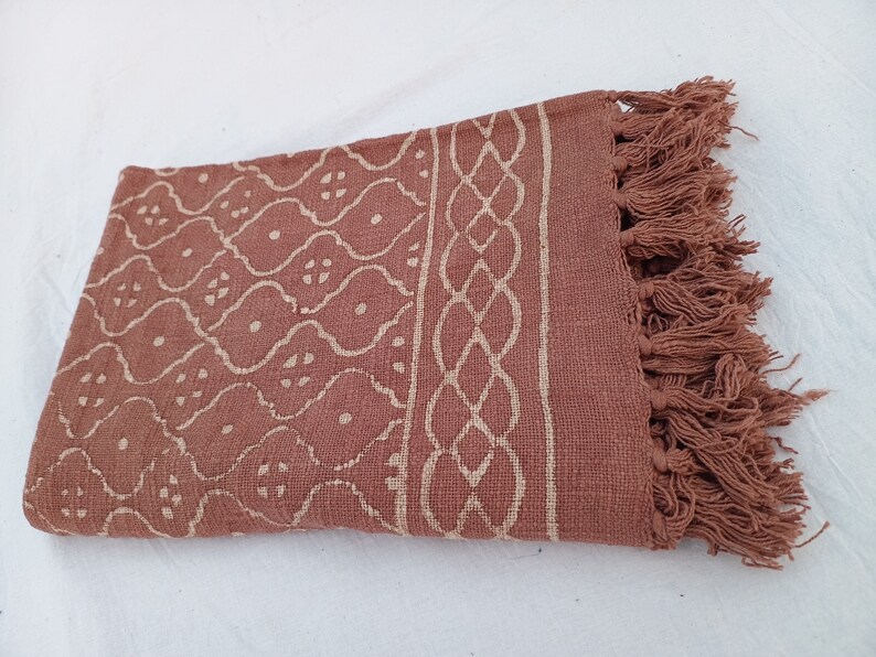 May include: A brown cotton throw blanket with a white geometric pattern and fringe trim.