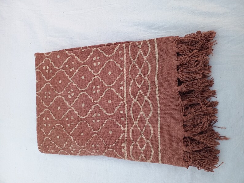 May include: A rust-colored cotton throw blanket with a white geometric pattern and fringe on the edges.