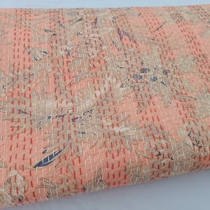May include: A peach-colored quilt with a floral pattern in beige, red, and navy blue. The quilt features a repeating design of stylized flowers and foliage, with visible white stitching throughout. The overall aesthetic is vintage and handcrafted.