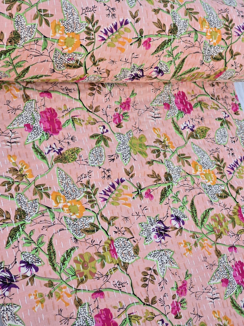 May include: A pink floral quilt with a repeating pattern of flowers and leaves in shades of pink, purple, green, and yellow. The quilt is hand-stitched with white thread, creating a textured surface. The overall design is a botanical theme.