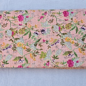 May include: A folded, floral-patterned quilt in shades of pink, green, yellow, and purple. The quilt features a repeating pattern of flowers and leaves, with visible stitching throughout. The edges are neatly finished.