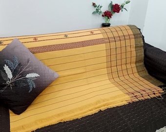 Puede incluir: Un textil amarillo con rayas marrones y adornos decorativos está drapeado sobre un sofá marrón oscuro. Un cojín decorativo con un diseño floral descansa sobre el sofá. Un jarrón de rosas rojas está en el fondo.