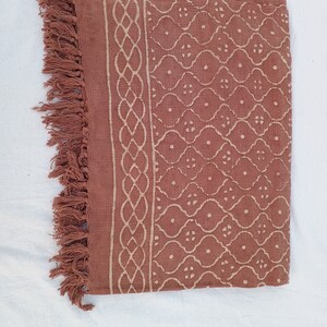 May include: A rust-colored throw blanket with a white geometric pattern and fringe trim.