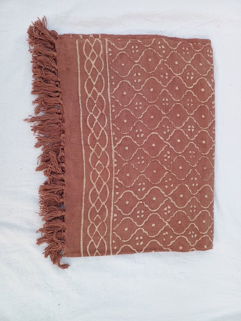 May include: A rust-colored throw blanket with a white geometric pattern and fringe trim.