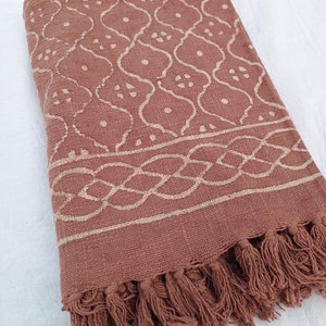 May include: A brown cotton throw blanket with a white geometric pattern and fringe trim.