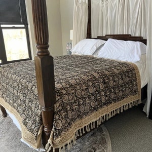 May include: A black and cream patterned bedspread with a fringe border, draped over a wooden four-poster bed frame.