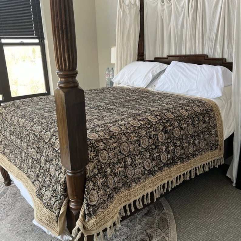 May include: A black and cream patterned bedspread with a fringe border, draped over a wooden four-poster bed frame.